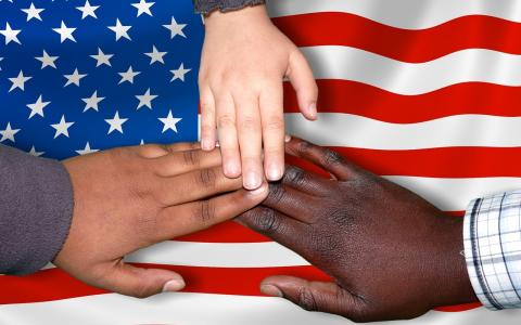 An American flag with three hands coming together. One white, one black, one brown