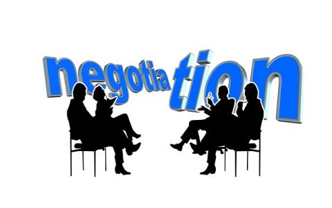 Two groups facing each other while sitting with the word negotiation in the background