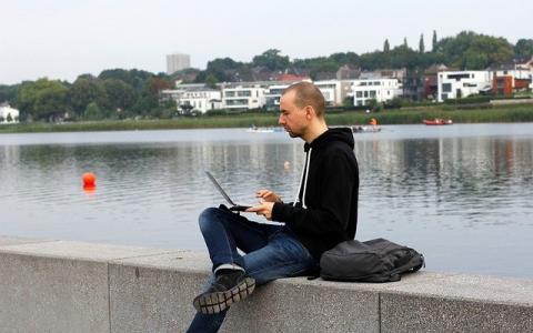 Person sitting next to a river working on their laptop