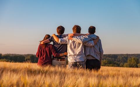 Four young people with arms around each other in an open field facing away from the camera