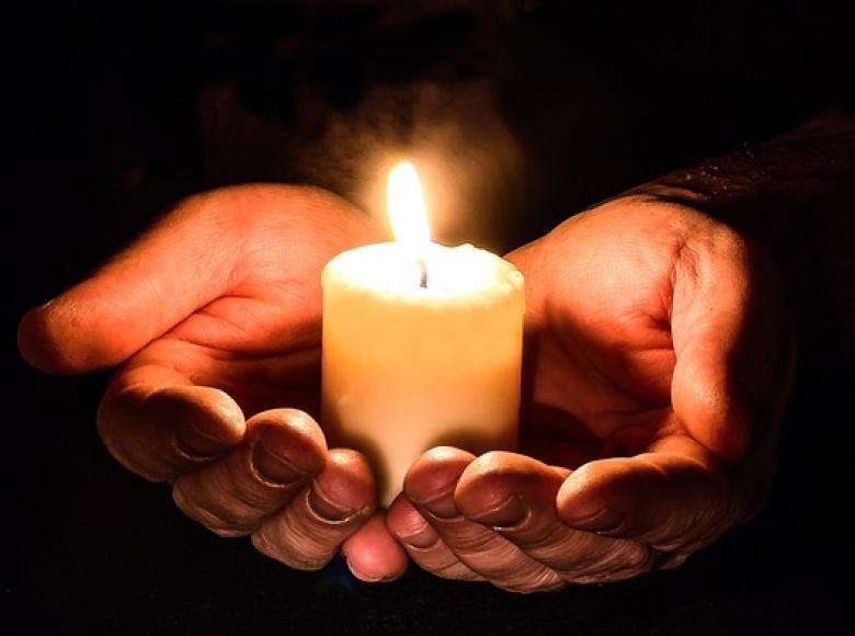Two hands holding a lit candle with a black background