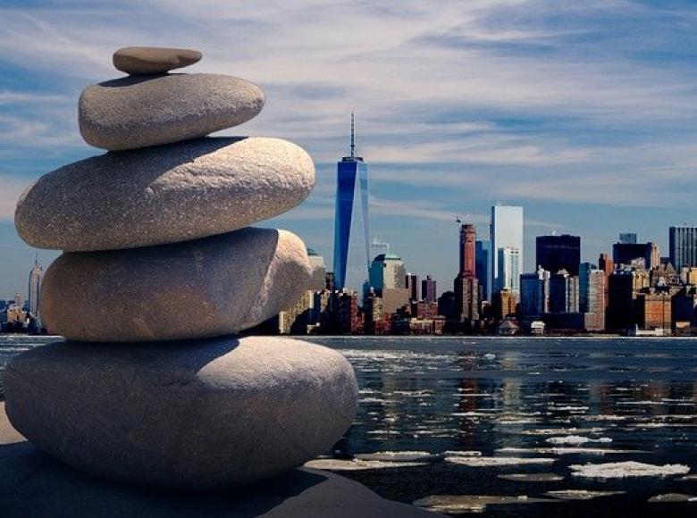 Five stones piles on top of each other in the foreground and a city skyline across water in the background