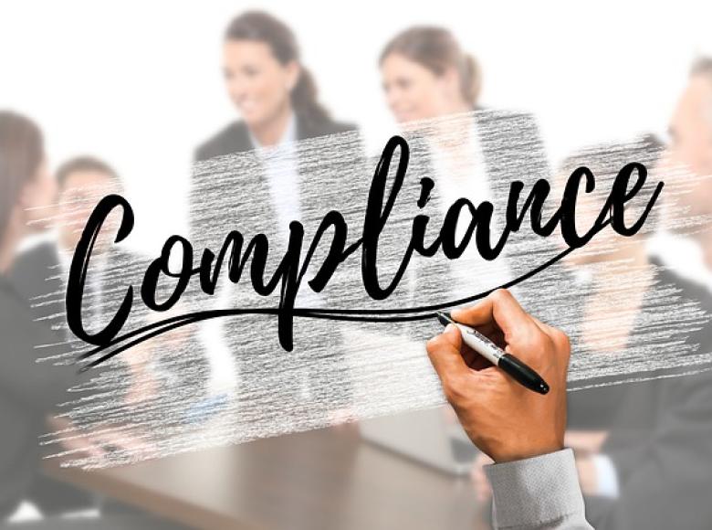 The word Compliance in cursive with a photo of others in the background