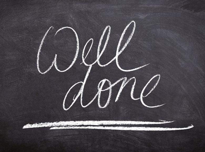 The words "Well done" with white chalk on a black board