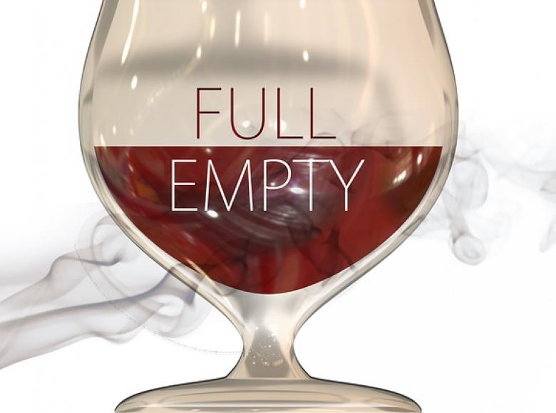A glass of red wine half full with the upper of the glass half labeled full and the lower half labeled empty