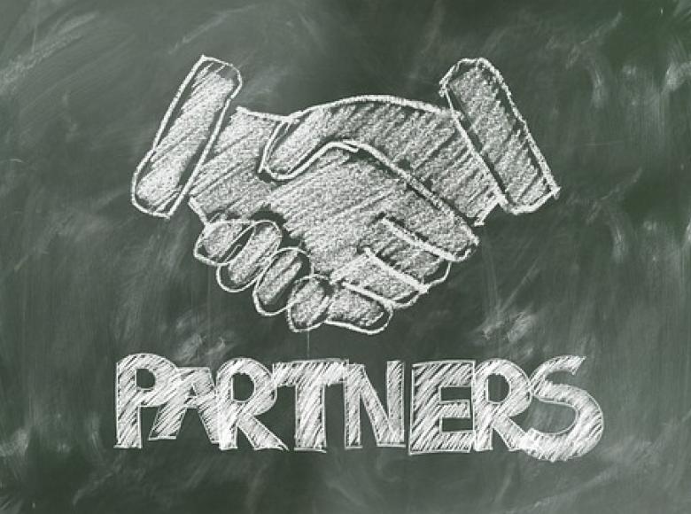 Two shaking hands with the word partners underneath drawn on a blackboard
