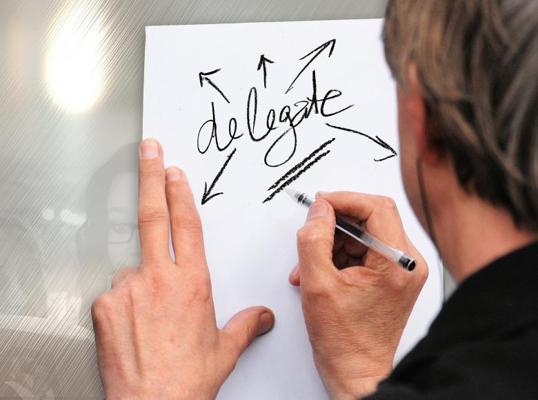 A person writing the word delegate on a piece of paper with arrows pointing away from the word