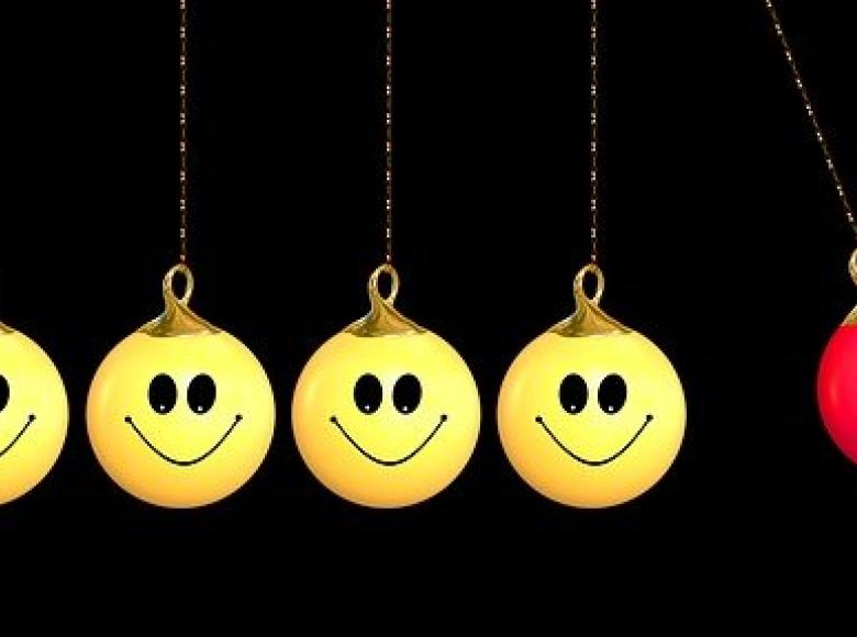 Four yellow smiley face hanging balls about to be hit by a red angry face hanging ball