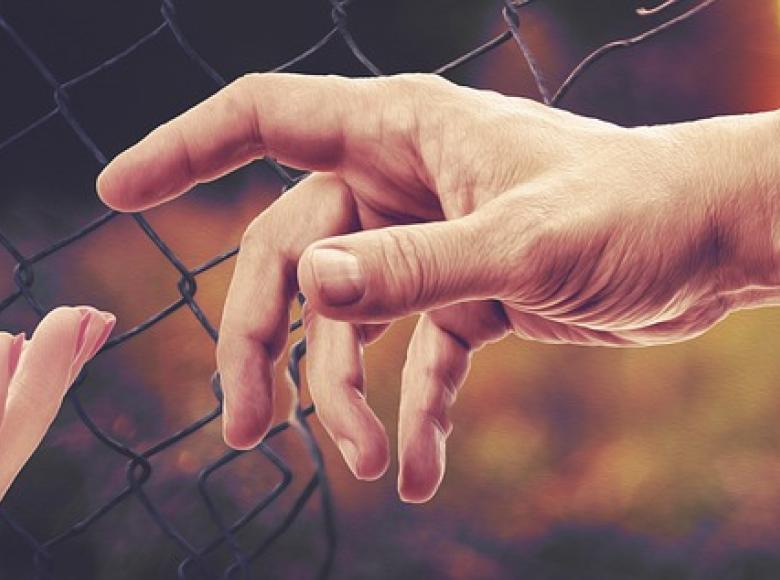 A small hand reaching up to a larger hand reaching through a fence