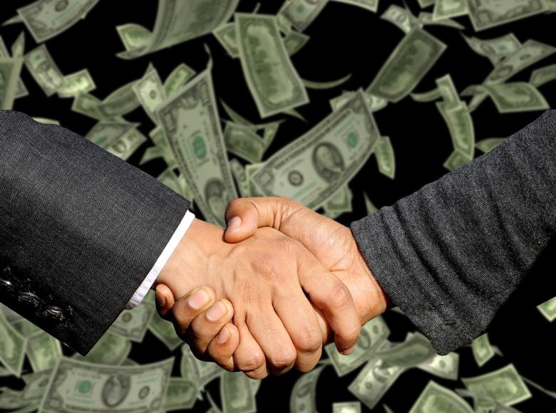 Two individuals shaking hands with money in the background