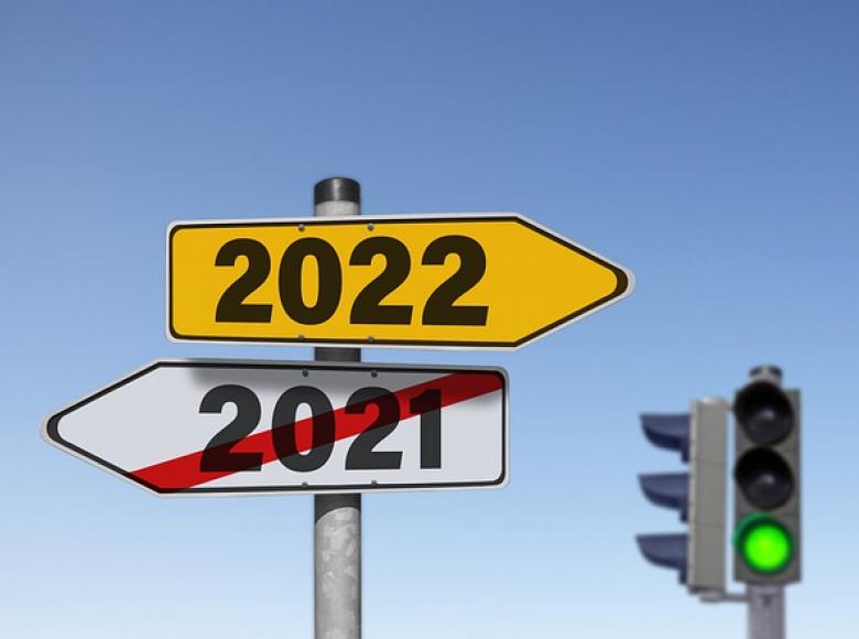 yellow 2022 sign pointing right with white 2021 sign and red international not line across it with a green stop light to the right