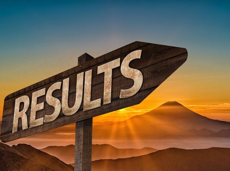 A sign with "RESULTS" printed on it pointing up to the right with a barren mountain sunset behind it 