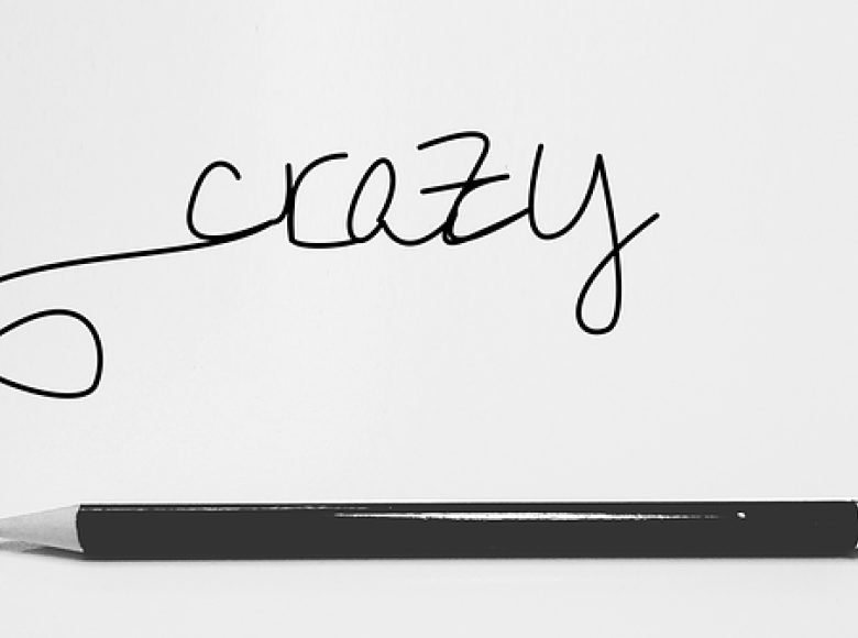 The word crazy in script hand writing written with a pencil and the pencil laying under the word