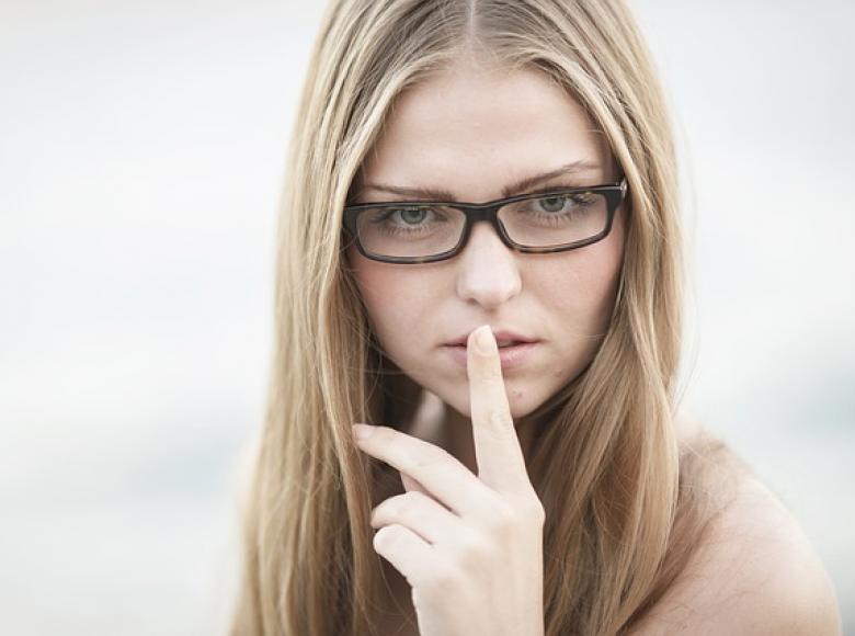 Woman with finger to mouth signalling quiet