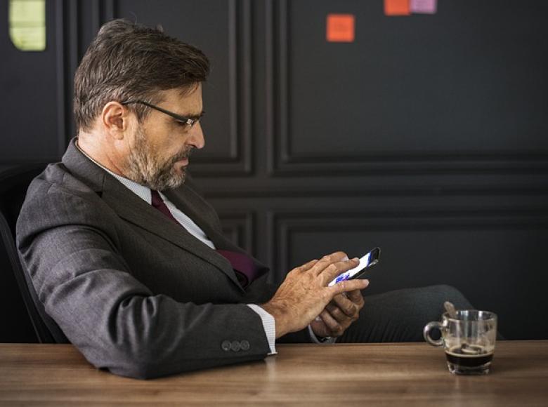 Man in suit sitting at desk looking at phone and texting