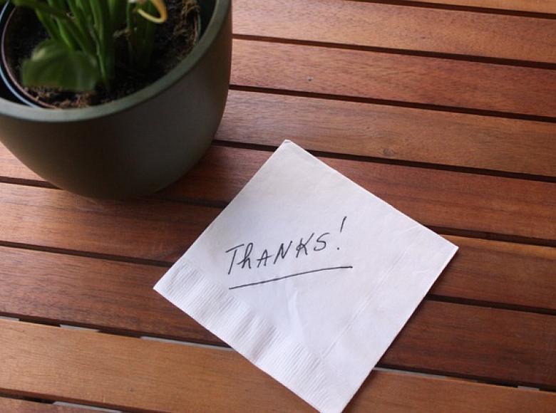 A hand written note on white paper stating "Thanks" on a desk next to a plant.